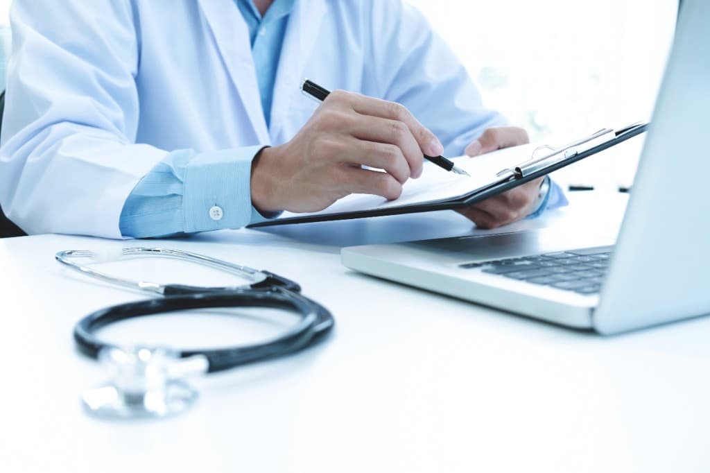 Medical professional documenting care at a desk with stethoscope and laptop